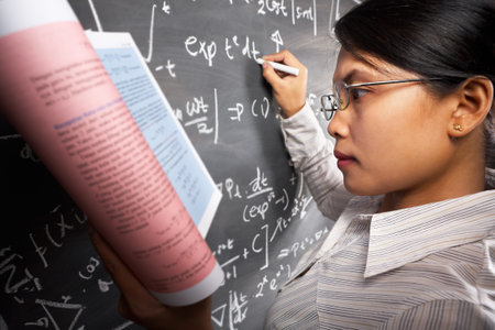 Female student working on difficult equation on blankboard while holding book