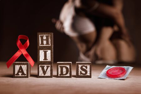 Red ribbon, HIV - AIDS word and condom with people doing free sex on dark area as backgroundの写真素材