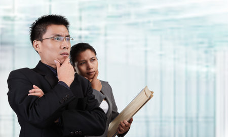 Two Asian business people thinking and looking to empty space with blur  glass window background. **** PS: stitching the length of background to fit for banner composition ****の写真素材