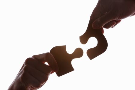 Hands try to solve the uncommon shape puzzle, taken in silhouette against bright white backgroundの写真素材