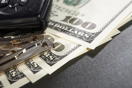 Keys and alarm device on top of several one hundred dollar billsの写真素材