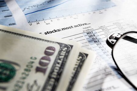 Glasses and dollar bills over stock echange data paper. Very shallow depth of fieldの写真素材