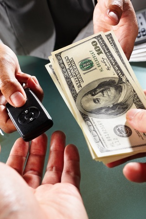 Two people on car transaction, one holding US dollar bills and another holding car alarm deviceの写真素材