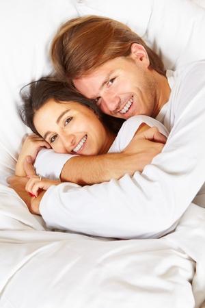 Happy couple showing their romance on fully covered white bedの写真素材