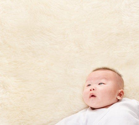 Chinese baby boy looking up to empty copy space of fur bed. 