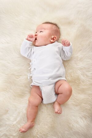 Chinese boy lying on fur bed alone in white outfitの写真素材