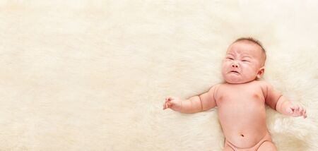 Crying Chinese baby boy on fur bed with lots of copy space. の写真素材