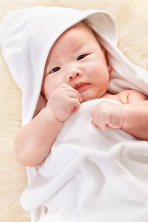 Close up phto shoot of Chinese baby boy covered with white blanket on fur bedの写真素材