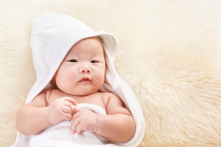 Close up phto shoot of Chinese baby boy covered with white blanket on fur bedの写真素材