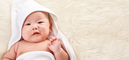 Close up photo shoot of Chinese baby boy covered with white blanket on fur bed, with gesture like saying hello to camera. の写真素材