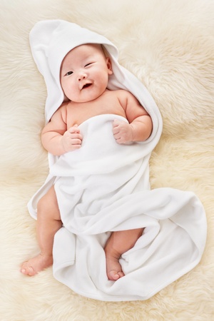 Chinese baby boy covered with white blanket on fur bedの写真素材