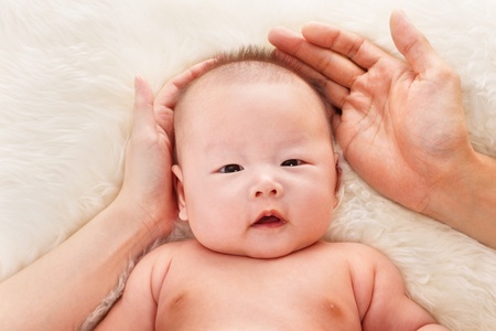 Chinese baby boy being protected and loved by his parent, with their hands around him.の写真素材