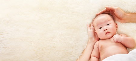 Chinese baby boy being protected and loved by his parent, with their hands around him.の写真素材