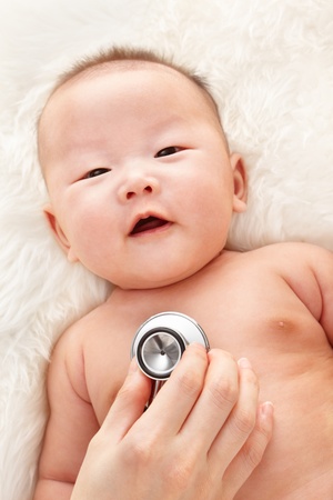 Chinese baby boy being examined by pediatrician on fur bedの写真素材