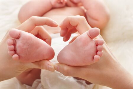 mother's hand holding her baby's feet, with fur bed cover on background, with fur bed cover on backgroundの写真素材