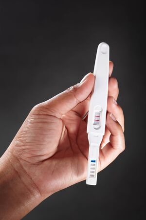 Hand holding a pregnancy test device, against dark backgroundの写真素材