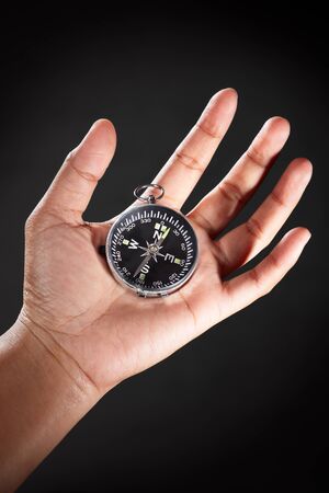 Hand holding a compass, against dark backgroundの写真素材