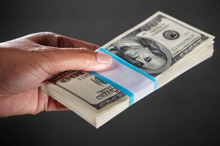 Hand holding a stack of 100 dollar bills, against dark backgroundの写真素材