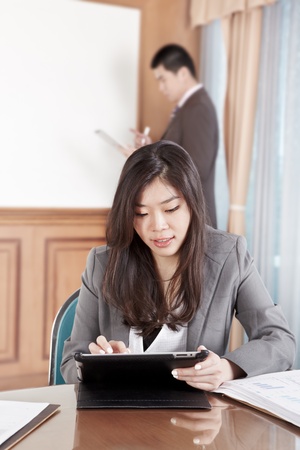 Chinese businesswoman busy working with her tablet while businessman on background busy preparing presentationの写真素材
