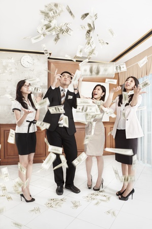 Group of business people happily looking at the thrown dollar bills in the officeの写真素材