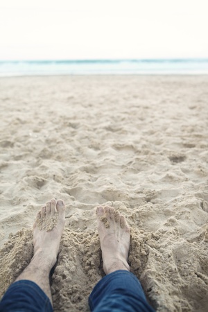 Man's feet relaxing on the beach sandの写真素材