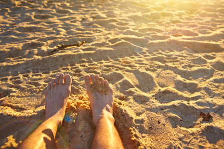 man's feet relaxing on the sandy beach. there is lens flare on the pictureの写真素材