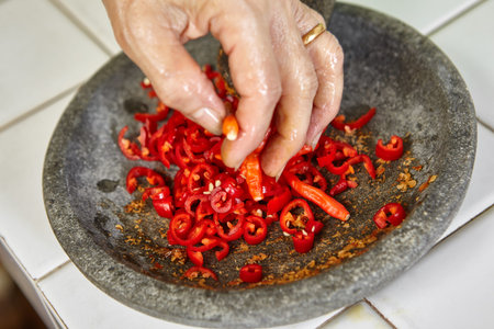 Making sambal, special chilli food in Indonesia to eat together with another meal to add hot and spice flavour, all the ingredient crushed using stone pestle on stone mortarの写真素材