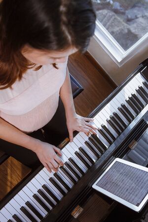 Pregnant Asian young woman playing piano for the babyの写真素材