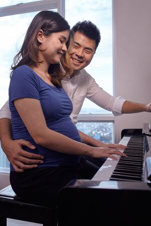 Asian young couple playing piano fot the baby in the wombの写真素材
