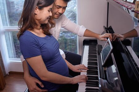 Asian young couple playing piano fot the baby in the wombの写真素材