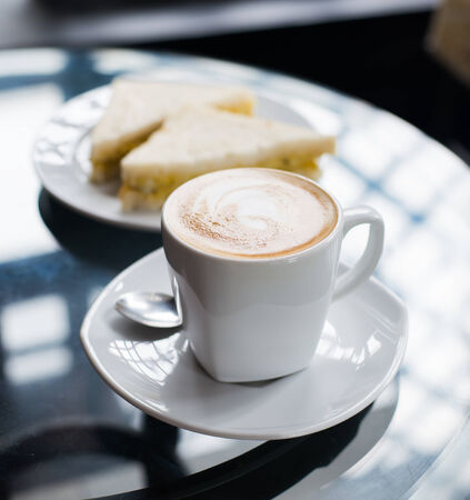 cup of coffee and sandwich on glass tableの写真素材