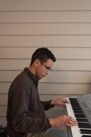 Side view of a young man playing an electric keyboard, hands wide apart, looking down, copy space,...