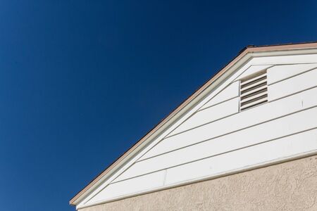 Generic house view of side and roof edge, stucco and vinyl with attic ventilation set against a deep blue sky, copy space, horizontal aspectの写真素材