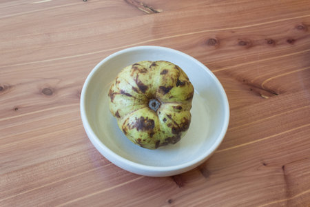 Centered view of a ripe Annona cherimola cherimoya fruit in a shallow dish, wood background, copy...