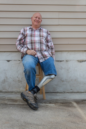 Smiling amputee man, prosthetic leg forward, seated, copy space, vertical aspectの写真素材