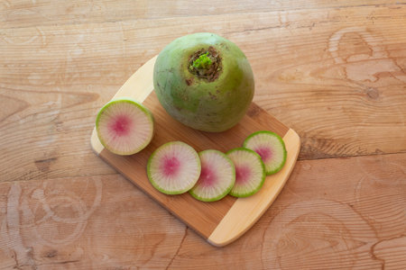 Large watermelon radish and radish slices on a bamboo cutting board, vintage wood table, horizontal...