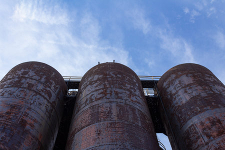 Extreme upward view of three large metal tanks against a blue sky, copy space, horizontal aspect