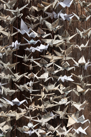 Close view of folded origami paper cranes hanging from strings, old wood packground, vertical aspectの写真素材