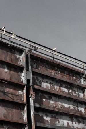 Huge bolted steel wall with pipes along the top, gray sky, vertical aspect
