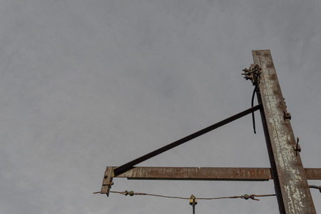 Rusted metal stanchion with outrigger and wires before gray sky copy space, horizontal aspectの写真素材