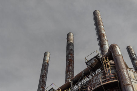 Extreme upward view of smokestacks on blast furnaces in an industrial steel mill, grey sky,...