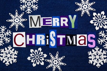 Merry Christmas text word collage surrounded by white paper snowflakes, multi colored fabric on blue denim, winter holiday, horizontal aspectの写真素材