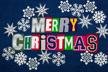 Merry Christmas word text collage with many white paper snowflakes, multi colored fabric on blue denim, winter holiday, horizontal aspectの写真素材