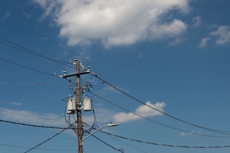 Power pole and lines with transformers and street light, blue sky with clouds, horizontal aspect