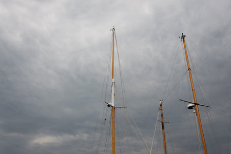 Trio of ship masts, rigging but no sails, against threatening skies with storm clouds, horizontal...