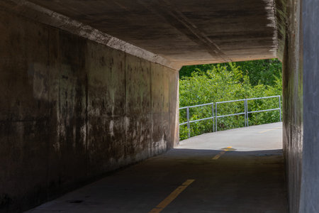 Bike path tunnel under roadway, sharp curve and railing beyond, horizontal aspect