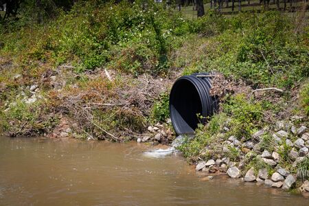 Black plastic drainage culvert pipe releasing water into a stream, environmental safety issue, horizontal aspectの写真素材
