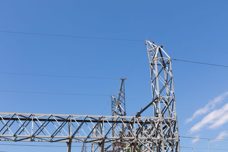 Metal trusses supporting electrical wires and insulators viewed from below, blue sky with clouds,...