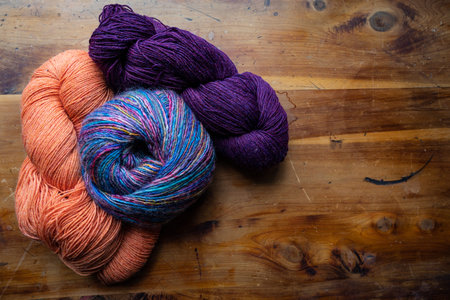 Three skeins of richly colored yarns gathered on an old wooden background, old world handcraft...