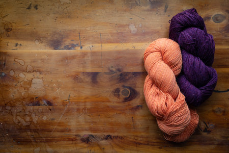 Two twisted skeins of yarn in purple and orange on an old wood table top, knitting and crochet...
